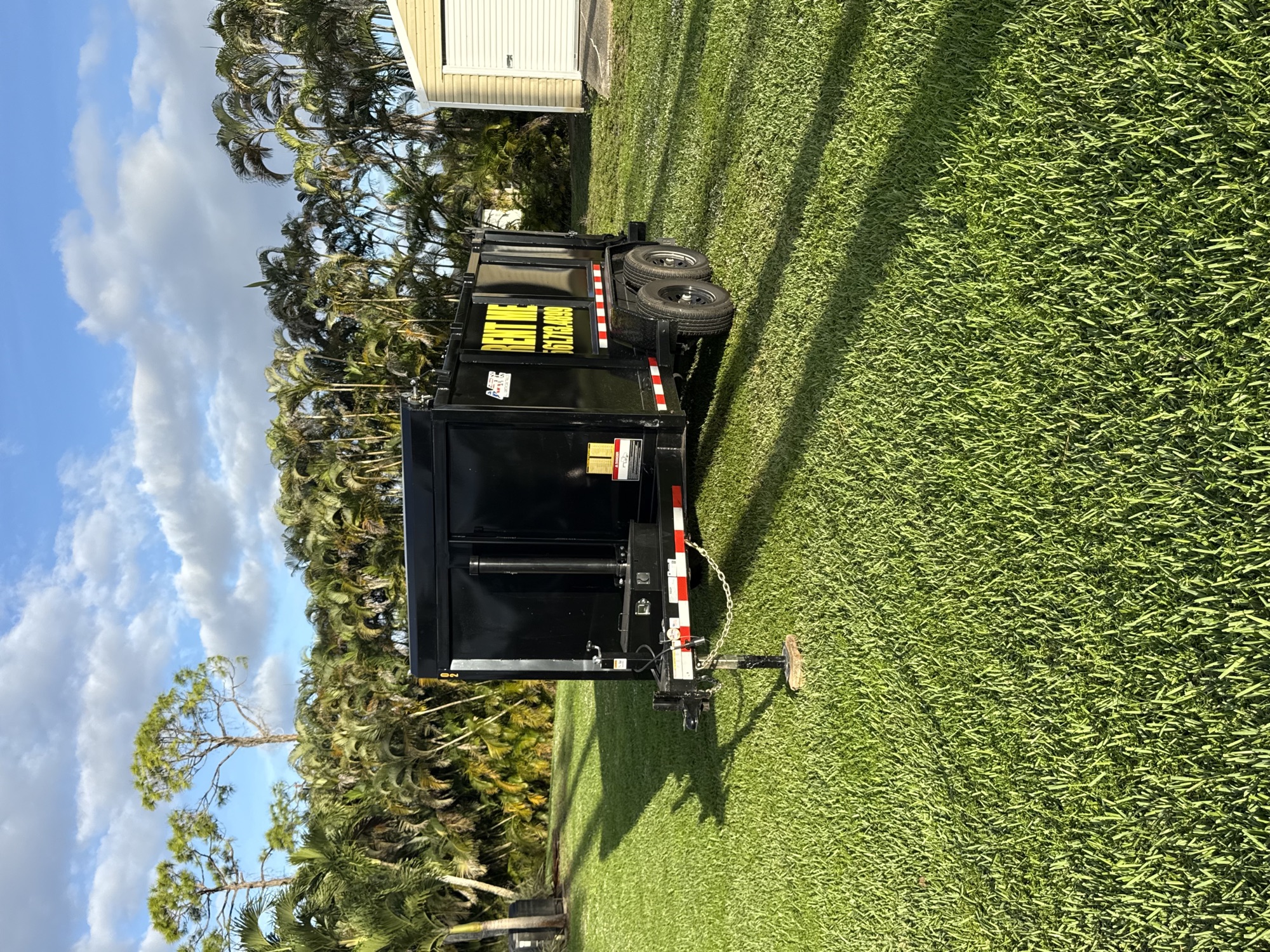 Dump trailer parked on a lawn lined with palm trees